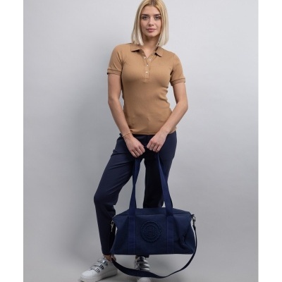 Mulher com polo castanha, calças azul-escuro e mala azul escuro em fundo branco