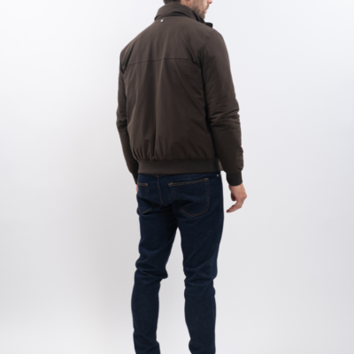 Homem de costas a usar casaco castanho, calças de ganga azuis e ténis brancos