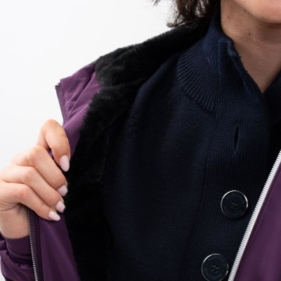 Mulher com casaco roxo de pelo preto e camisola azul escura com botões