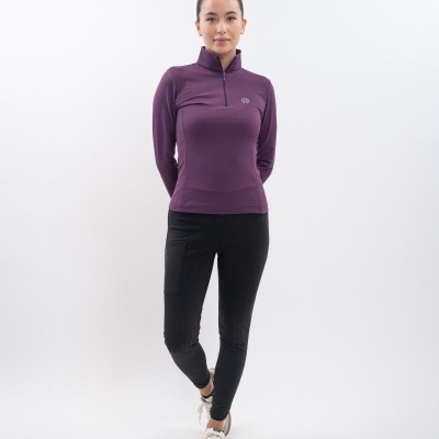 Mulher com top roxo de manga comprida, calças pretas justas e ténis brancos em fundo branco.