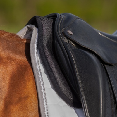 Sela preta em pele sobre manta branca e pelo castanho de cavalo