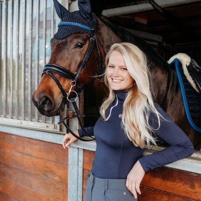 Mulher com roupa de equitação ao lado de cavalo em estábulo