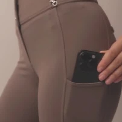 Mulher a mostrar calças justas taupe com bolso para telemóvel, em estúdio