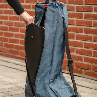 Mala de transporte azul com bolso frontal preto e fecho vermelho junto a parede de tijolos