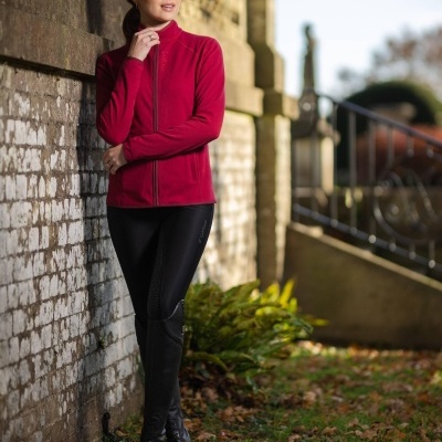 Mulher de casaco vermelho e calças pretas junto a parede exterior