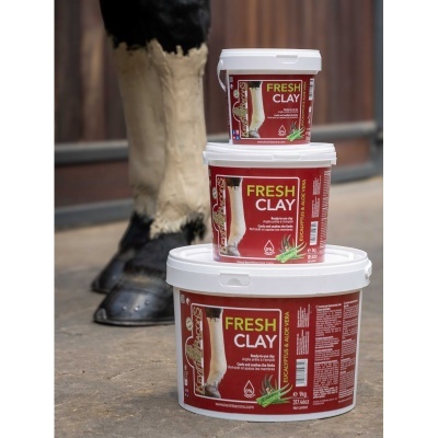 Três recipientes de argila para cavalos Fresh Clay com rótulos vermelhos, empilhados junto à perna de cavalo