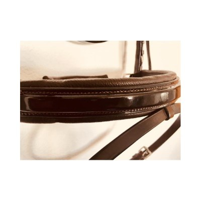 Rédea de couro castanho com costuras, pendurada junto à parede clara