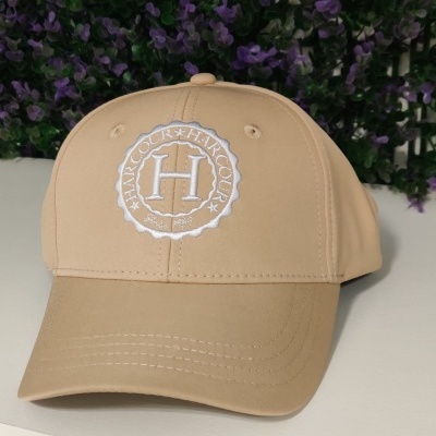 Boné bege com bordado branco letra H, com flores roxas ao fundo