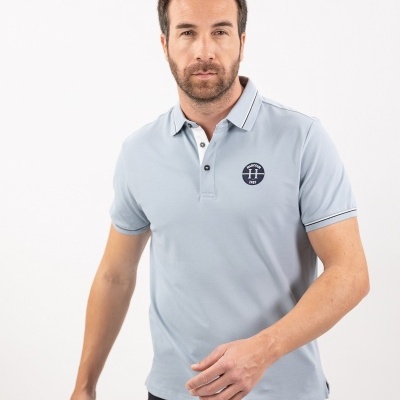 Modelo masculino com polo azul claro de algodão e logótipo 'TH' no peito.