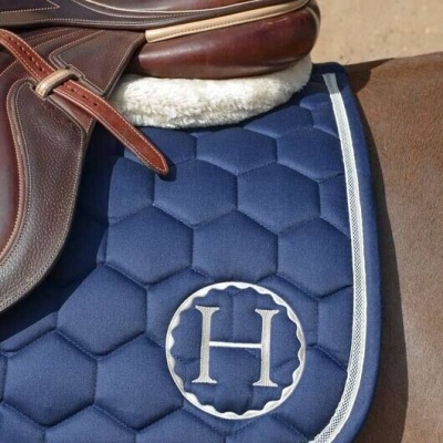 Sela de pele castanha sobre zoador azul acolchoado com letra H bordada