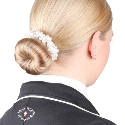 Mulher loira com coque e acessório de pérolas veste casaca preta bordada