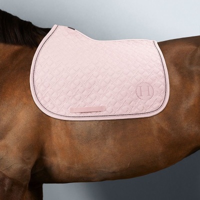 Sela rosa clara acolchoada com a letra H aplicada sobre cavalo castanho