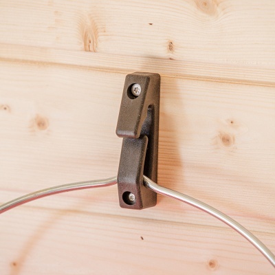 Gancho metálico castanho fixado em parede de madeira clara com aro metálico pendurado