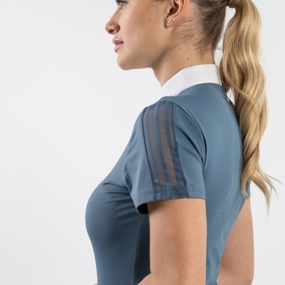 Mulher vestindo camisola azul com gola branca e riscas nas mangas, cabelo em rabo de cavalo, fundo branco