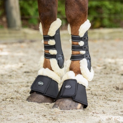 Proteções pretas acolchoadas com pelúcia branca nas pernas de cavalo castanho no chão de areia