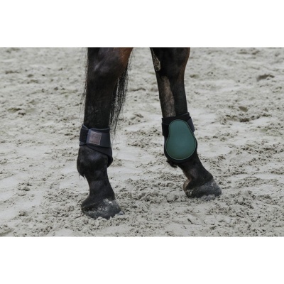 Patas traseiras de cavalo preto com proteção verde e fixaçãp de velcro preta na areia