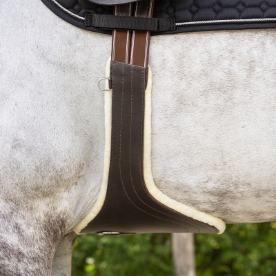 Cinta para cavalo em pele castanha com pelo sintético creme, fivelas metálicas e tiras marrons com riscas brancas sobre pelo de cavalo cinzento