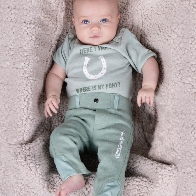 Bebé vestido com conjunto verde claro de roupa macia sentado sobre superfície felpuda bege