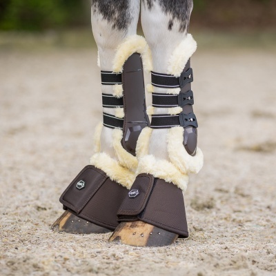 Botas de proteção castanhas com pelúcia bege para cavalos em superfície de areia