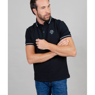 Homem com polo preta de algodão e jeans azuis sobre fundo cinzento