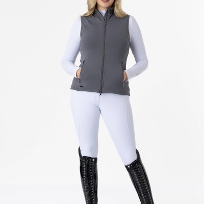 Mulher com colete cinza, camisa branca, calças brancas e botas pretas em fundo branco