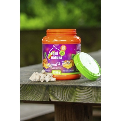 Frasco de suplemento alimentar Equi Natura Natural & Tasty Leckerli com tampa verde aberto sobre mesa de madeira ao ar livre