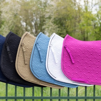 Mantas para sela de equitação em várias cores penduradas numa vedação verde ao ar livre