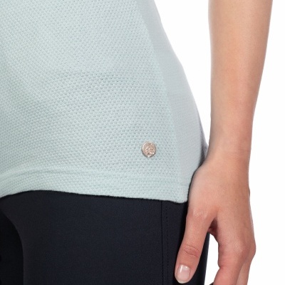 Detalhe de t-shirt verde água com textura e pequeno emblema metálico sobre calças pretas