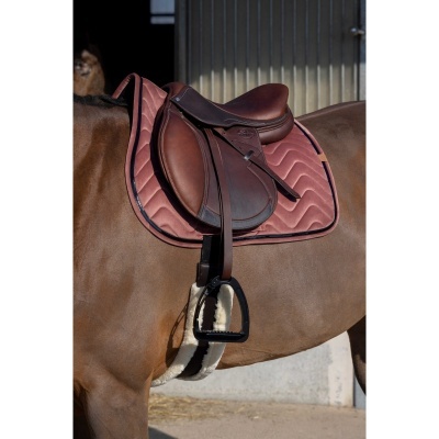 Sela de couro castanho e manta cor de rosa em cavalo numa área de estábulo