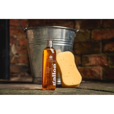 Frasco de champô laranja com esponja amarela e balde metálico num chão de pedra