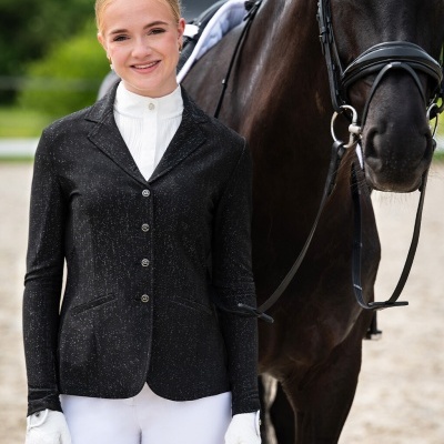 Mulher com roupa de equitação preta e branca junto a cavalo preto com sela e arreio.