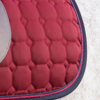 Manta de sela acolchoada vermelha com padrão hexagonal e contorno azul e vermelho sobre pelo de cavalo branco