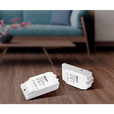 Dois dispositivos eletrónicos brancos sobre chão de madeira com sofá azul e mesa baixa ao fundo