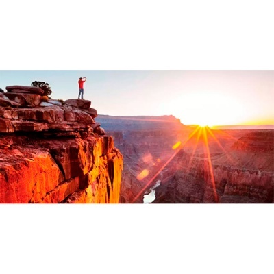 Pessoa em cima de rocha vermelha num canyon durante o nascer ou pôr do sol