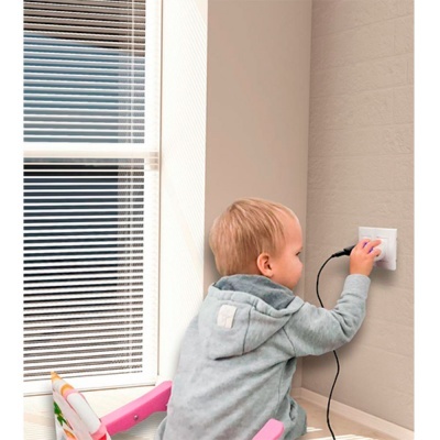 Criança mexendo numa tomada elétrica perto de janela com persianas