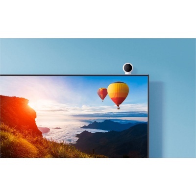 Televisor montado numa parede azul com imagem de paisagem e balões de ar quente, e uma pequena câmara branca no topo.