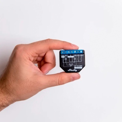 Módulo eletrónico preto com etiqueta azul e texto técnico nas mãos sobre fundo branco