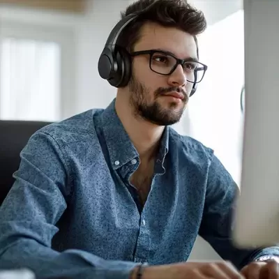 Homem com camisa azul, óculos e auscultadores a usar computador