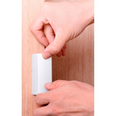 Mãos instalando dispositivo branco num móvel de madeira.