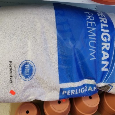 Saco de substrato Perligram Premium azul e branco sobre vasos laranja