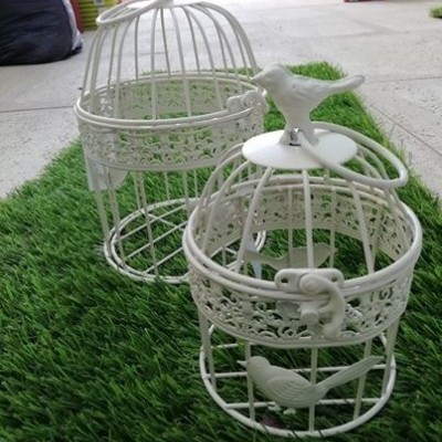 Duas gaiolas decorativas brancas em metal com figuras de pássaros sobre tapete verde
