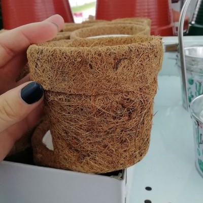 Vaso pequeno de fibra natural com textura áspera numa prateleira com vasos vermelhos e copos