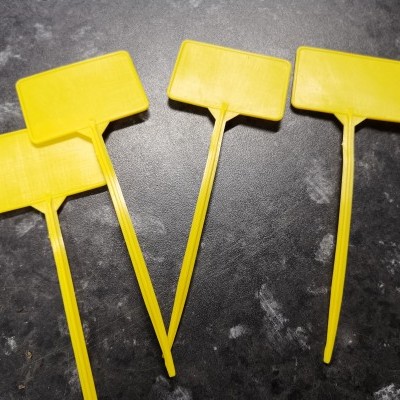 Quatro etiquetas de plástico amarelas retangulares com cabos longos sobre superfície escura