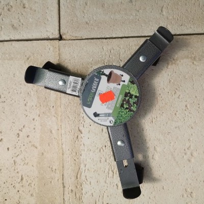 Suporte para churrasqueira em metal preto com três braços reguláveis sobre chão de azulejos bege.