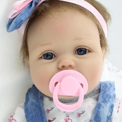 Boneca bebé realista vestida com jardineira azul e blusa branca floral com chupeta rosa