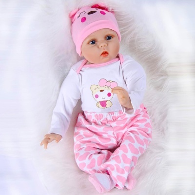 Boneca bebê com roupa rosa e branca deitada em superfície felpuda branca