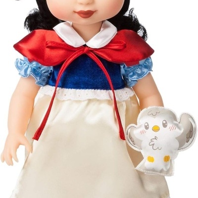 Boneca infantil vestida com vestido colorido e laço vermelho no cabelo, segurando brinquedo de pássaro