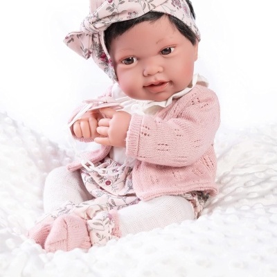Boneca bebé vestida com casaquinho rosa, calças florais e faixada floral rosa sentada