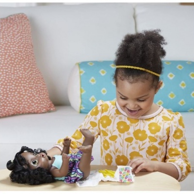 Menina brinca com boneca numa mesa com almofadas ao fundo