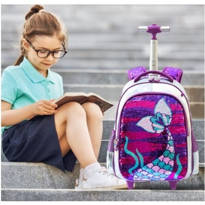 Mochila de lantejoulas com imagem de sereia e borboleta ao lado de criança sentada na escadaria